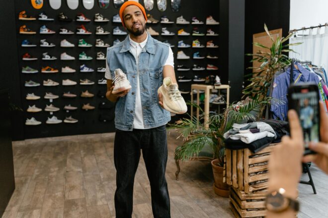 Man showcasing sneakers in a trendy retail fashion store with shoe wall display.
