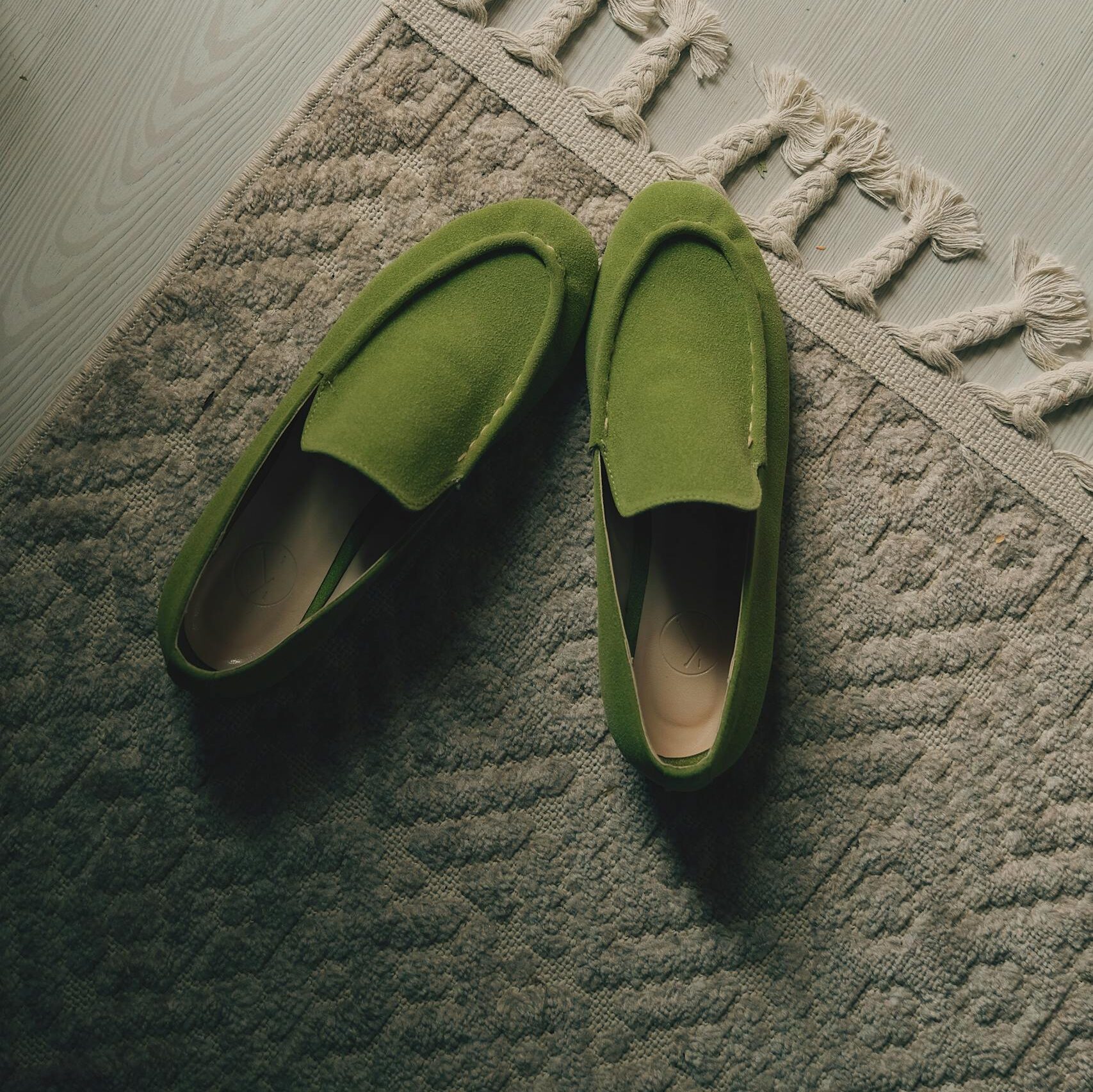 Top view of elegant green moccasins on a textured beige rug indoors.